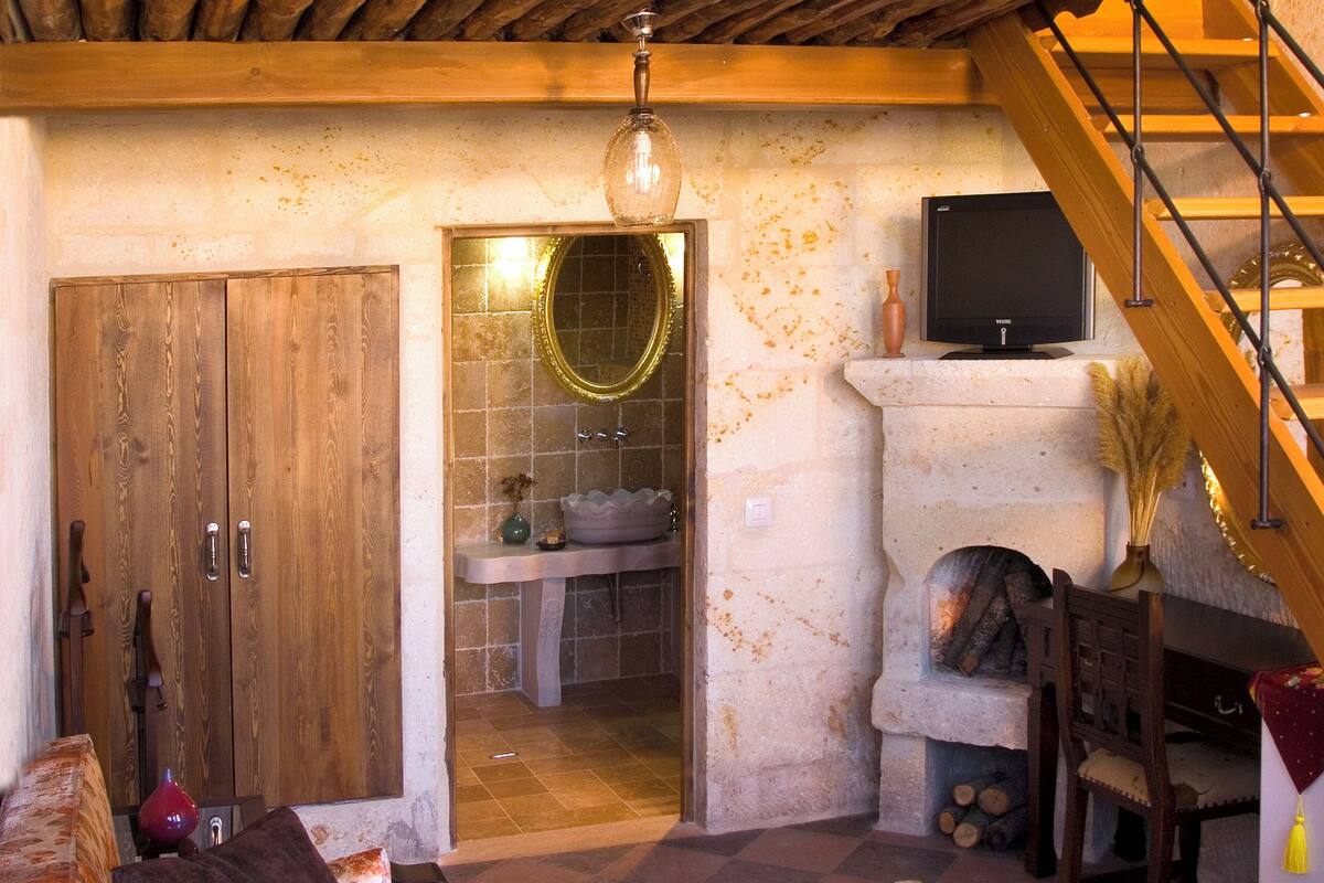 A rustic interior with a wooden staircase, a fireplace, a sofa, and a dining area.