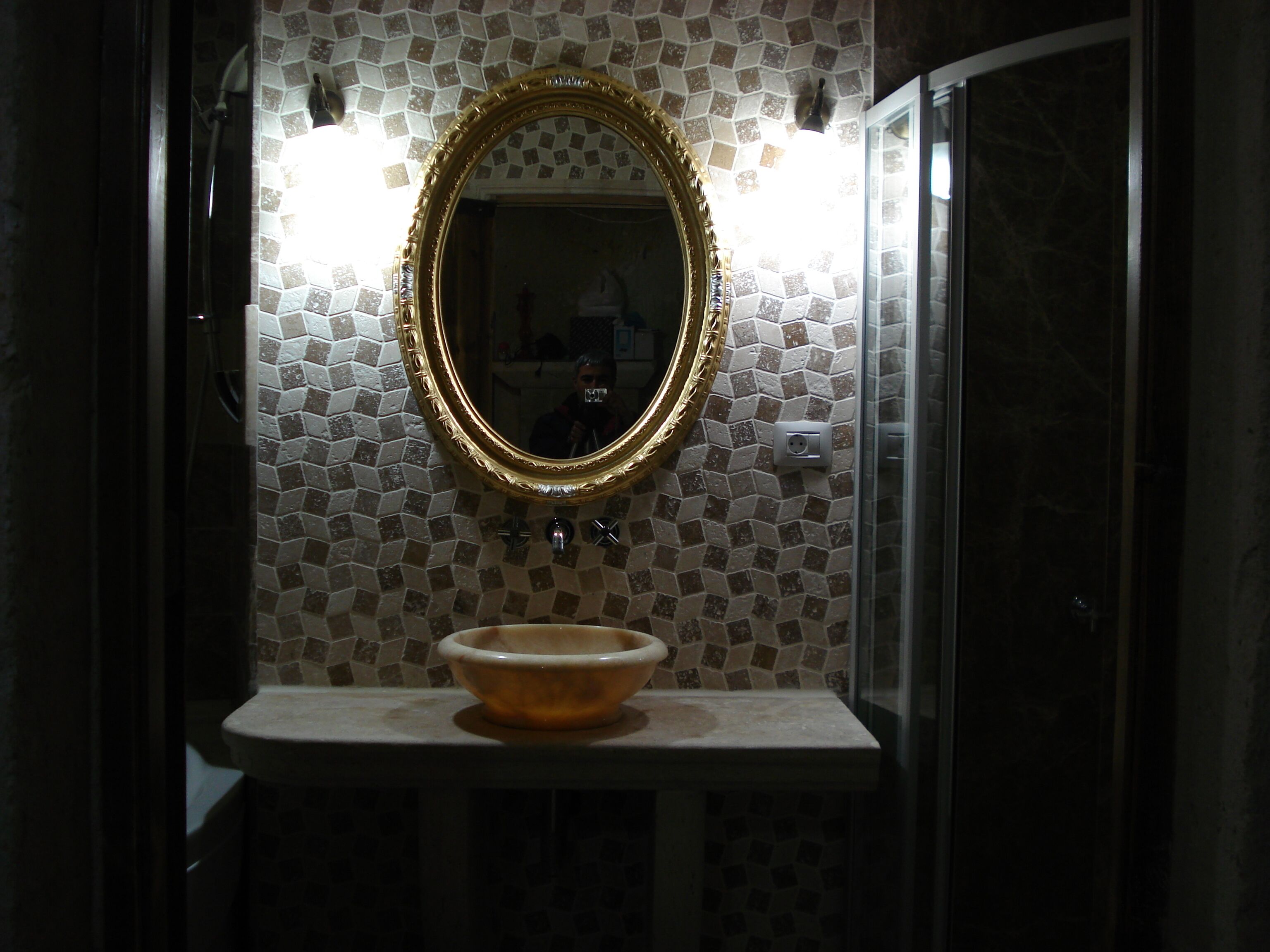 Un baño con pared de mosaicos, un espejo con marco dorado y un lavabo.
