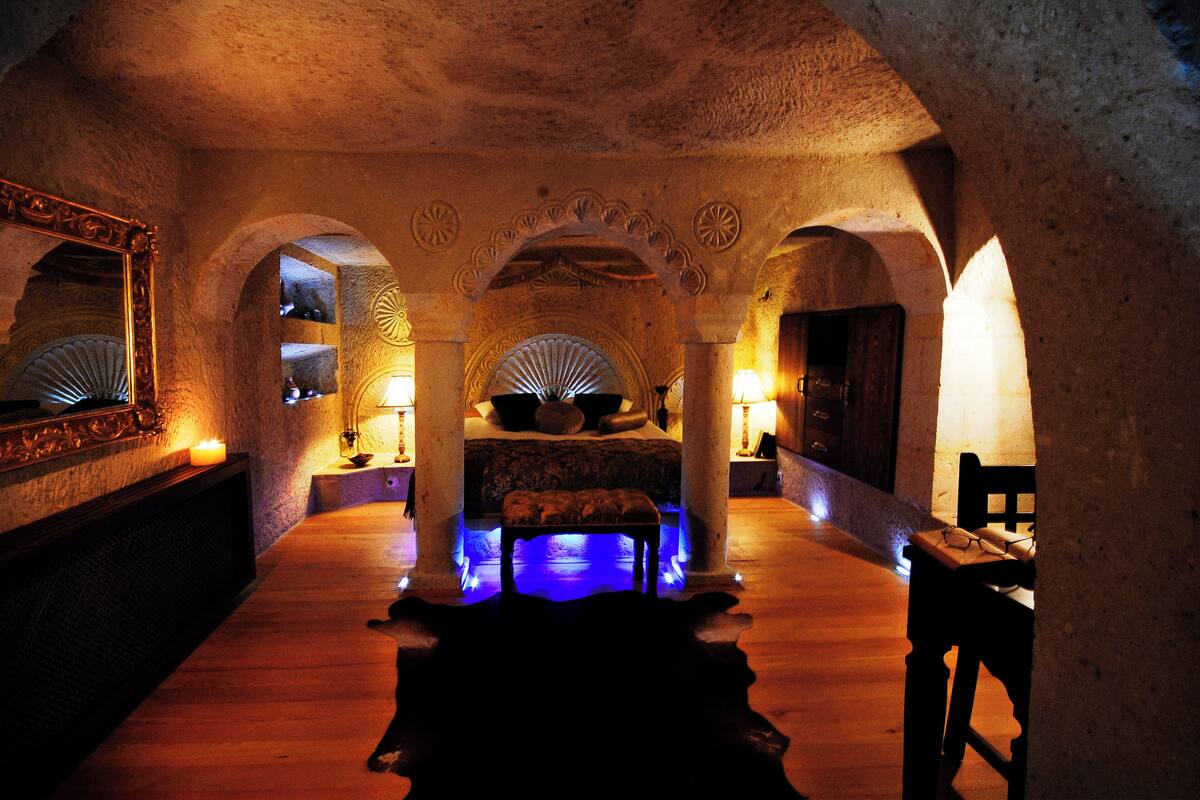 A dimly lit room with a bed, a bench, and a table with a lamp.