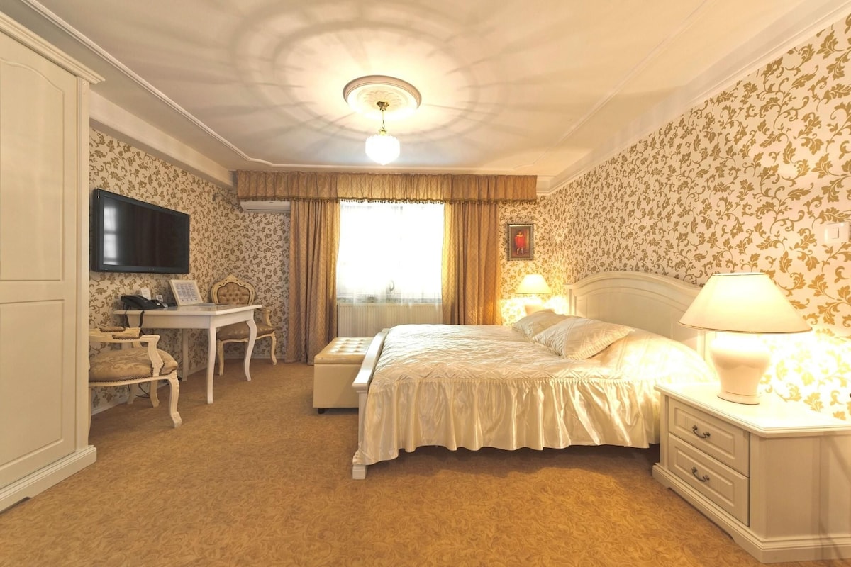 A bedroom with a bed, bedside table, lamp, TV, desk, chair, and wardrobe.