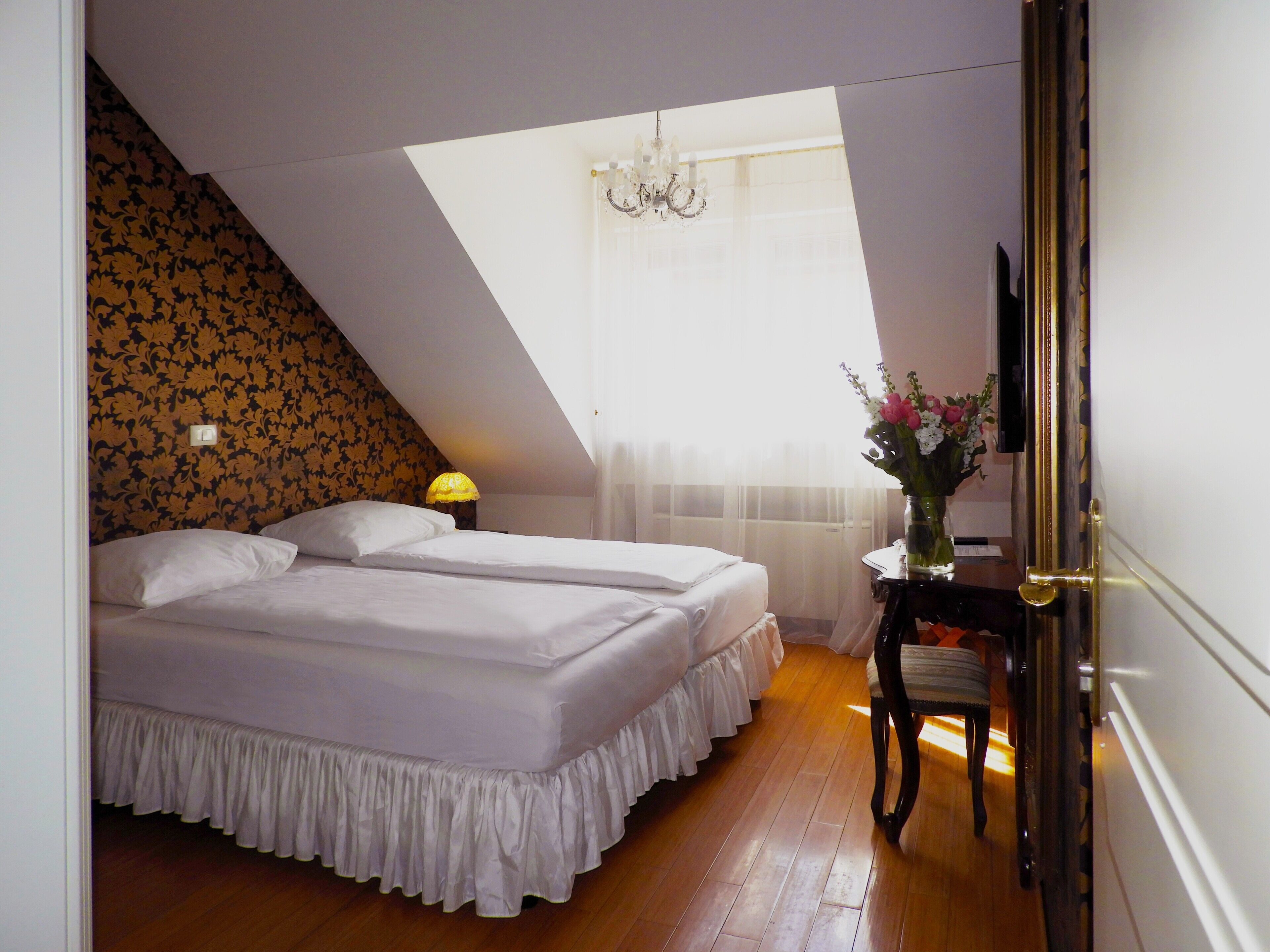 A bedroom with two beds, a chandelier, a vase with flowers, and a wooden floor.
