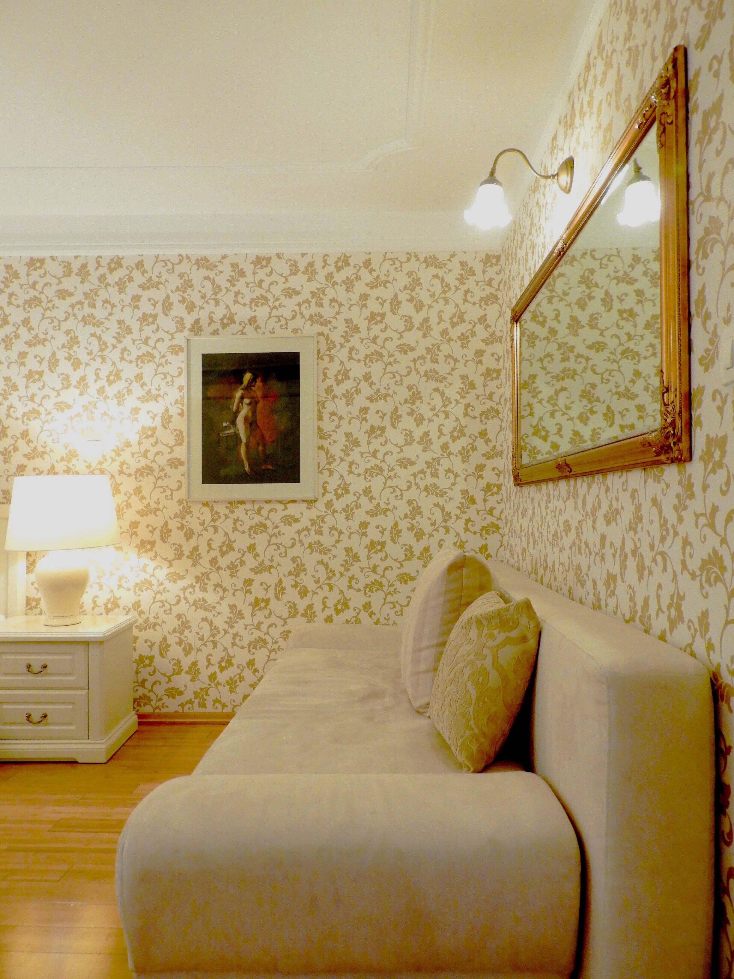 Une pièce avec un canapé blanc, une table de chevet avec une lampe, un tableau encadré au mur et un miroir.