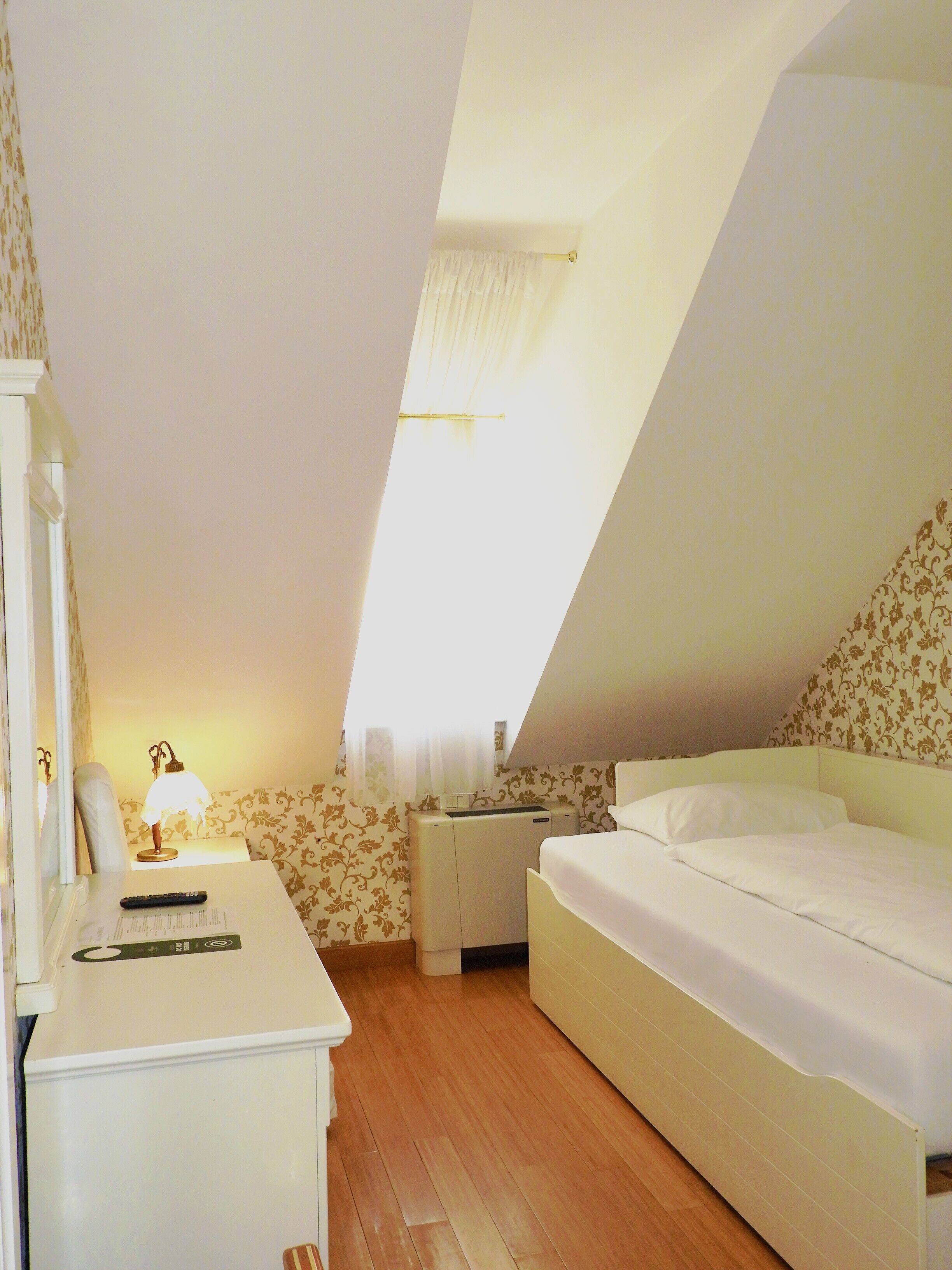 Une chambre à coucher avec un lit, un bureau, une lampe et une fenêtre.