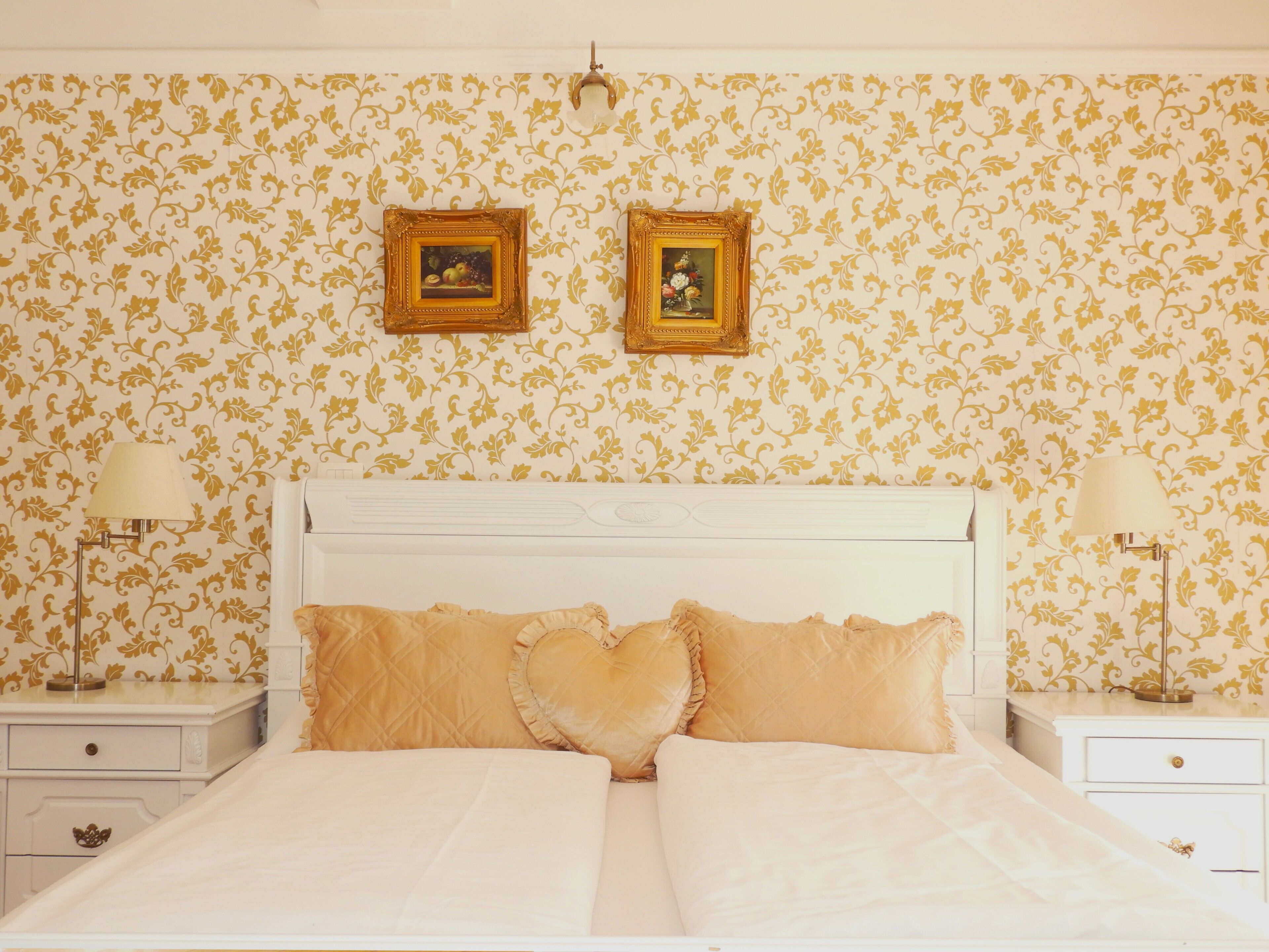A bedroom with a white bed, two nightstands, a white dresser, and two framed pictures on the wall.