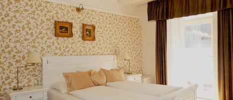 A bedroom with a large bed, two bedside tables, a chandelier, and floral wallpaper.