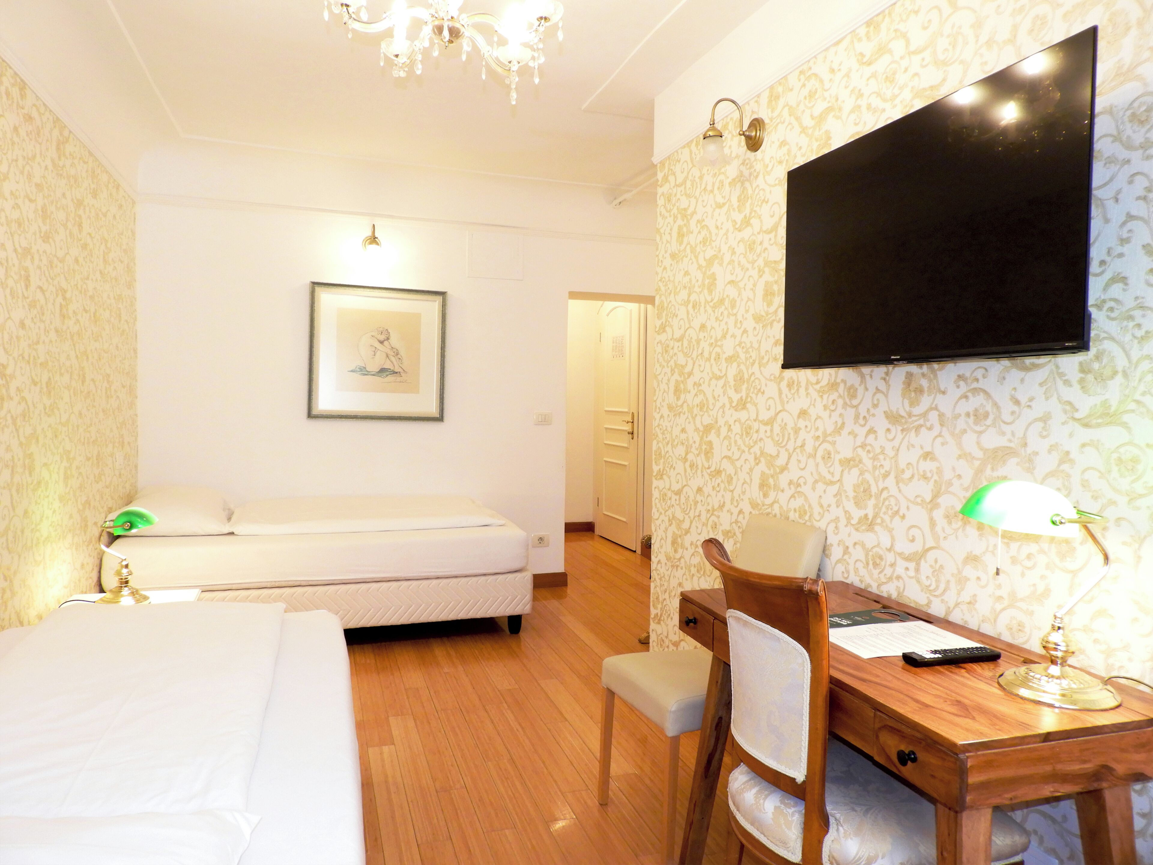 Ein Hotelzimmer mit Bett, Schreibtisch mit Stuhl, Wandfernseher und einem gerahmten Bild.