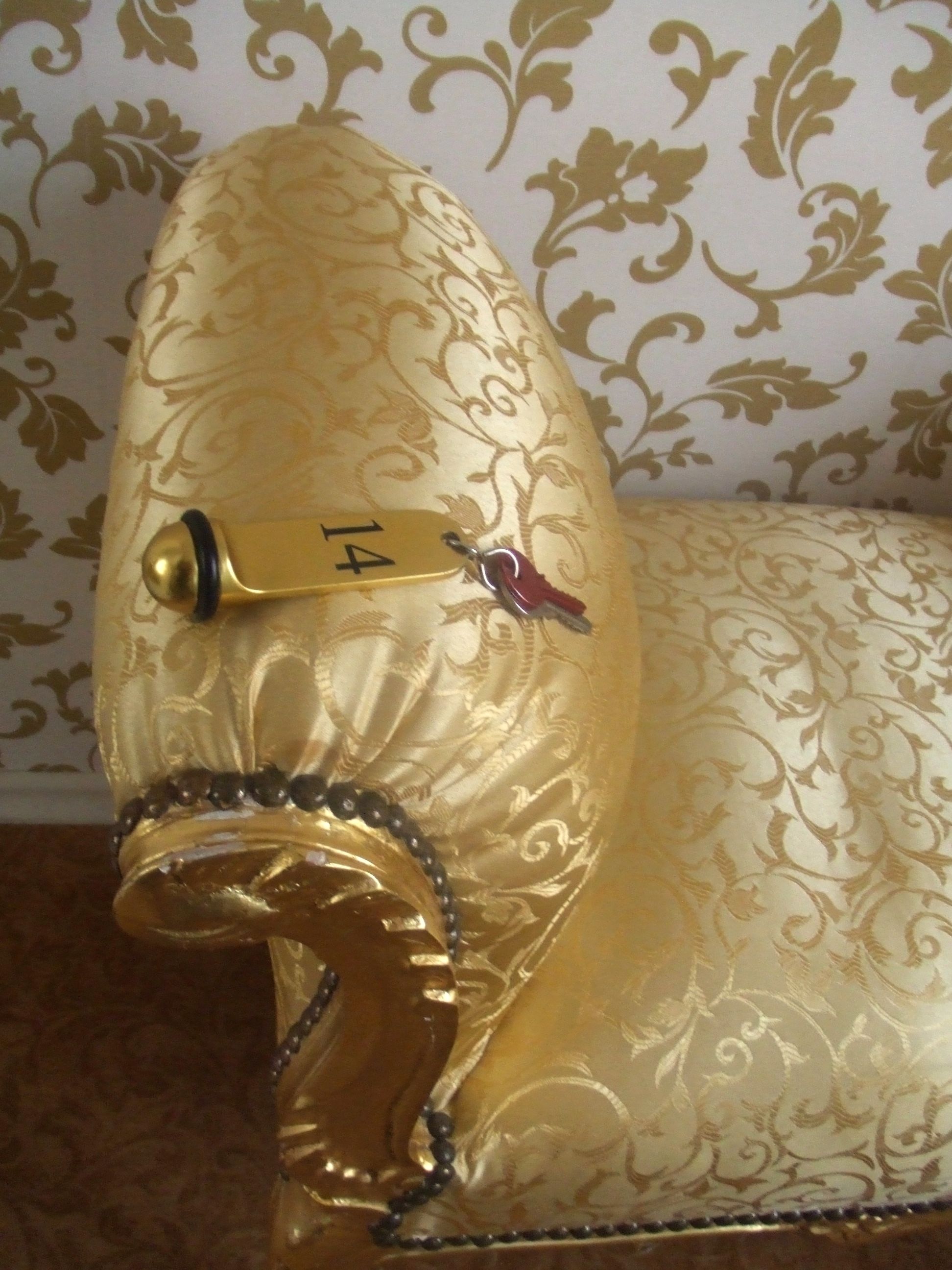 A golden, ornate chair with a number '14' on it, set against a patterned wallpaper background.