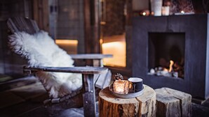 A cozy room with a fireplace, a wooden table with a candle, and a chair with a feather pillow.