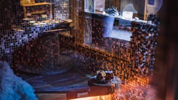 Experience a traditional setting with a mosaic-tiled floor and walls, a wooden bench, and a window offering a view.