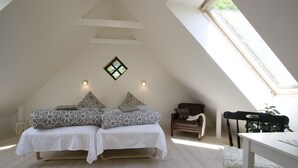 Un dormitorio con techo inclinado, tragaluz, cama con ropa de cama estampada, una mesita y una silla.