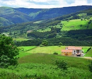 A rural house with a red roof, surrounded by green fields and hills. - Casona de la Ventilla (Laredo)