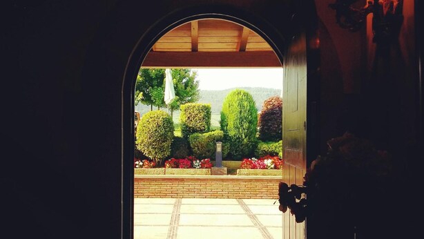 Un arco de entrada que da a un jardín con setos cuidados y un camino de ladrillo.