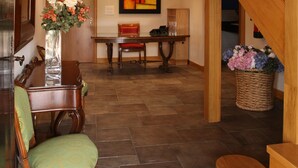 Una escalera de madera con barandilla, un comedor con mesa y sillas, y un jarrón con flores en el suelo.