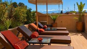A rooftop terrace with lounge chairs, a table, and a large umbrella. - Riad Dar More (Marrakech)