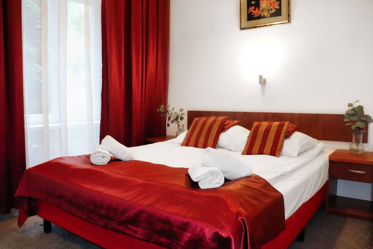 A neatly made bed with red and white bedding, a wooden headboard, and a nightstand with a vase of flowers.