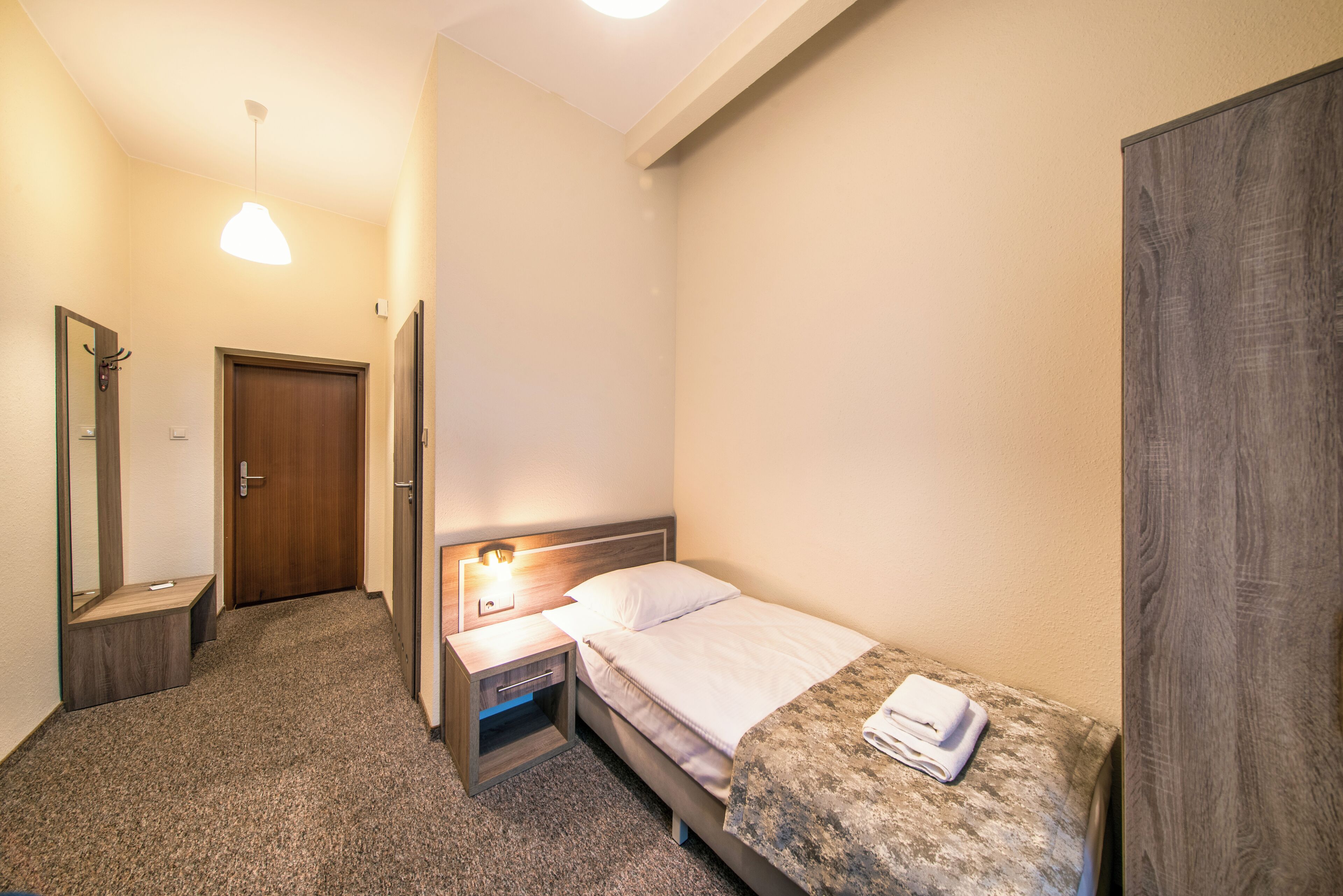 Une petite chambre à coucher, bien rangée, avec un lit simple, une table de chevet, une commode et un miroir.