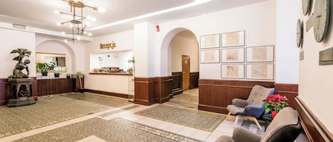 A lobby with a reception desk, seating area, and decorative elements like clocks and framed pictures.