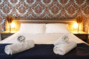 A neatly made bed with white linens and two rolled towels placed on the bed.