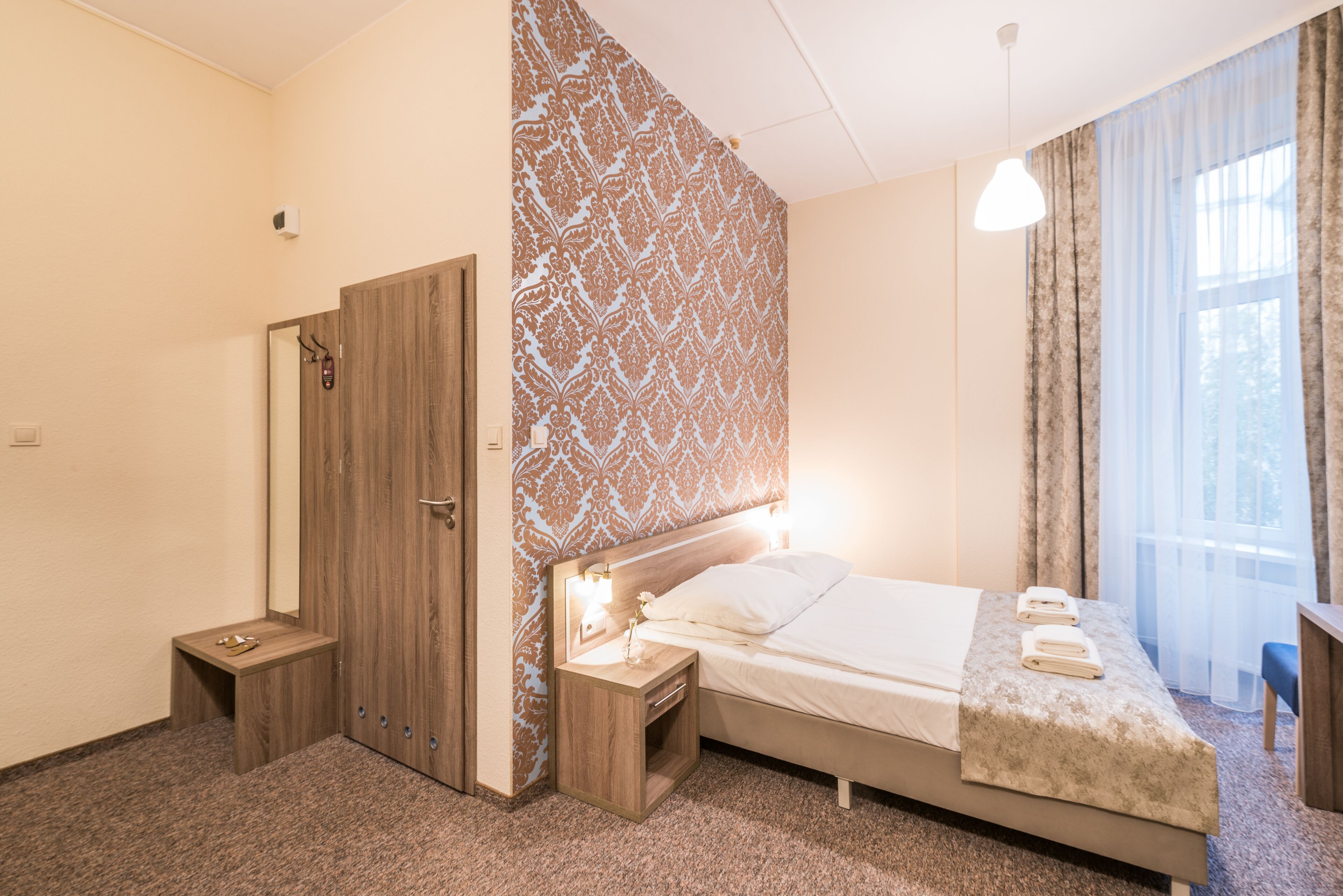 A hotel room with a bed, bedside tables, a wardrobe, and a window with curtains.