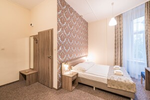 A hotel room with a bed, bedside tables, a wardrobe, and a window with curtains.