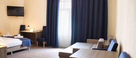 A hotel room with a bed, a desk, a computer, a TV, and a seating area with chairs and a table.