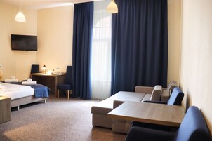 A hotel room with a bed, a desk, a computer, a TV, and a seating area with chairs and a table.