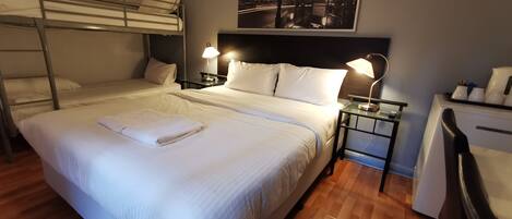A hotel room with a bunk bed, a single bed, a poster of the London Underground, a desk with a lamp, and a chair.