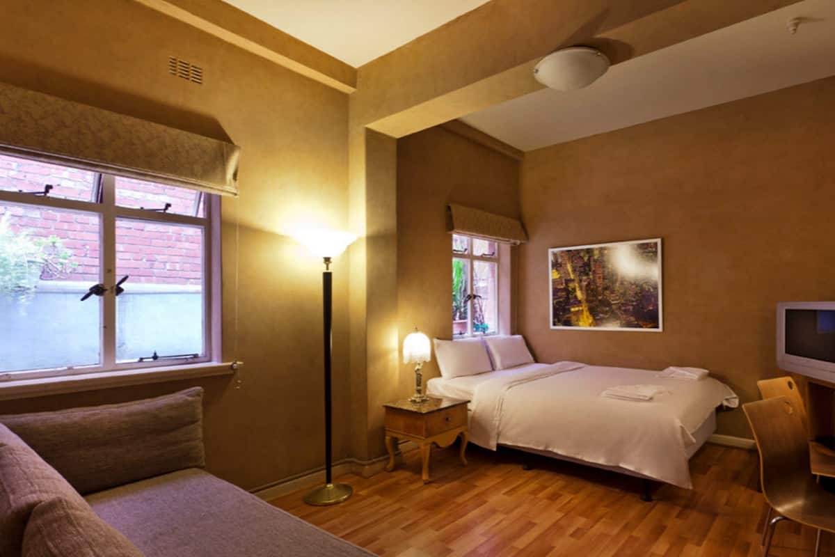 Une chambre d’hôtel avec un lit, une table de chevet, une lampe, une télévision et une vue sur la rue.