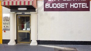 Fasaden på City Centre Budget Hotel, med en skylt, en entré och ett randigt solskydd.