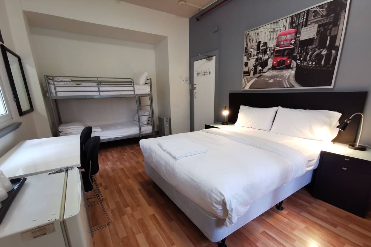 Une chambre d’hôtel avec un lit superposé, un lit simple, un bureau et une table de chevet avec une lampe.
