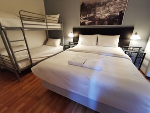 A hotel room with a bunk bed, a single bed, two bedside tables with lamps, and a cityscape view. - City Centre Budget Hotel (Melbourne)