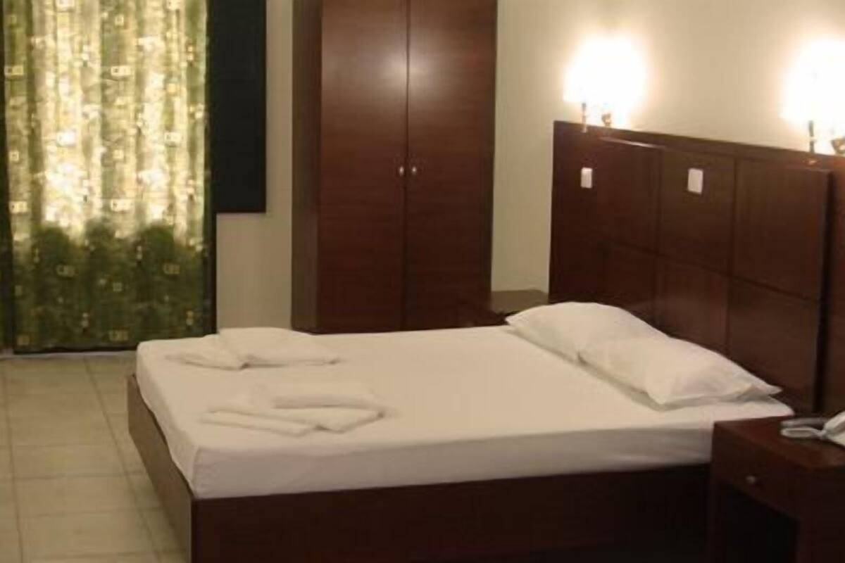 A hotel room with a bed, a chair, a wardrobe, and a curtain.