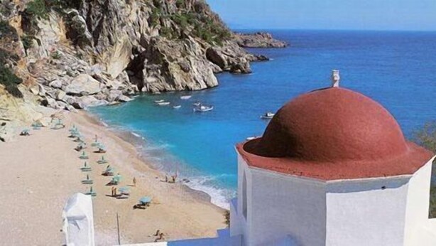 A coastal view with a beach, rocky cliffs, and a building with a red dome. - Kyra Panaghia (Karpathos)