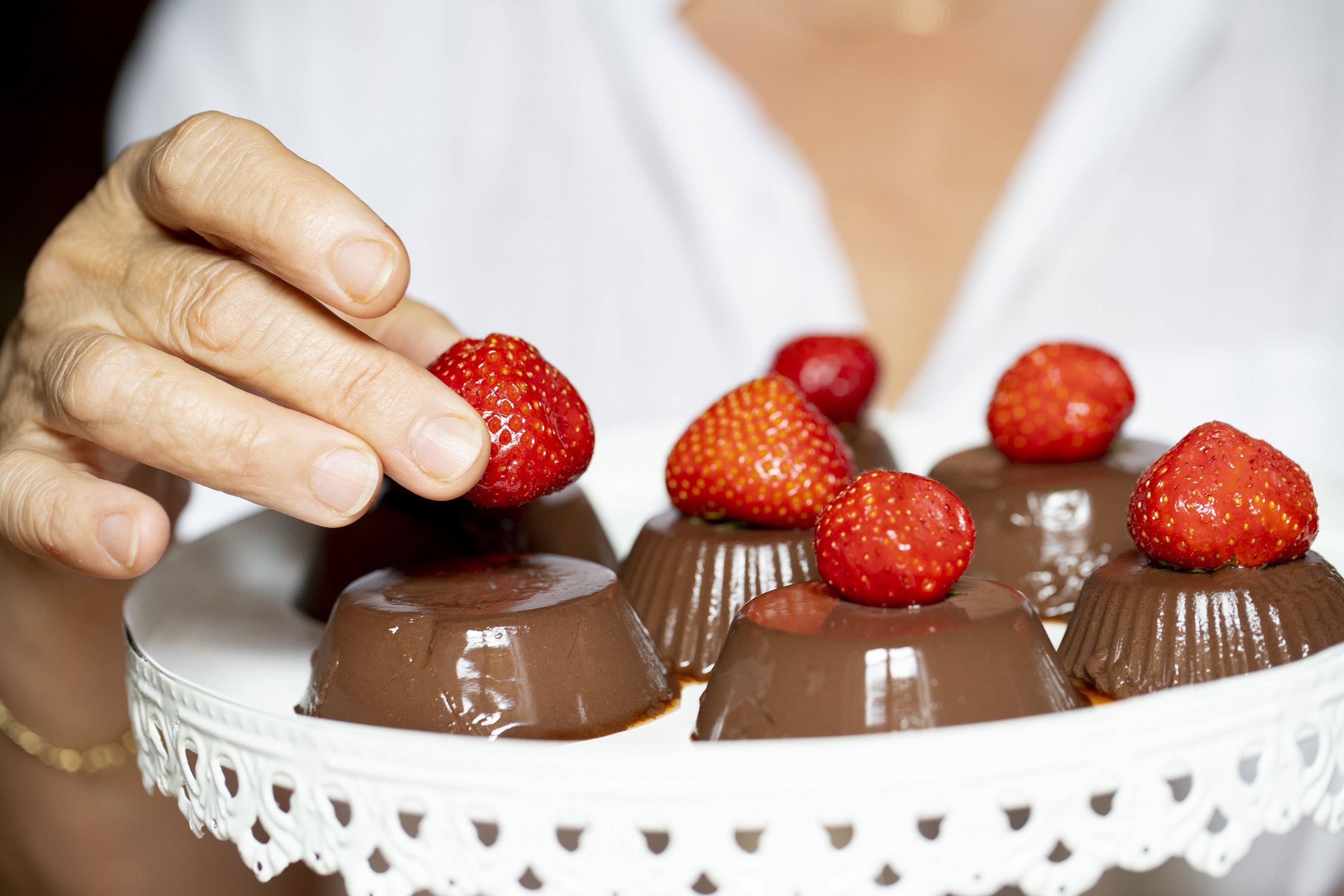 A white plate with chocolate desserts topped with strawberries.
