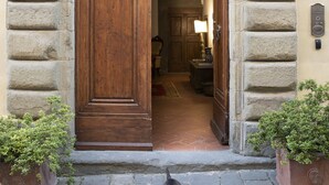 A stone archway leading to a wooden door, with a potted plant on the left and a lamp inside. - Palazzo Malaspina (Barberino Tavarnelle)