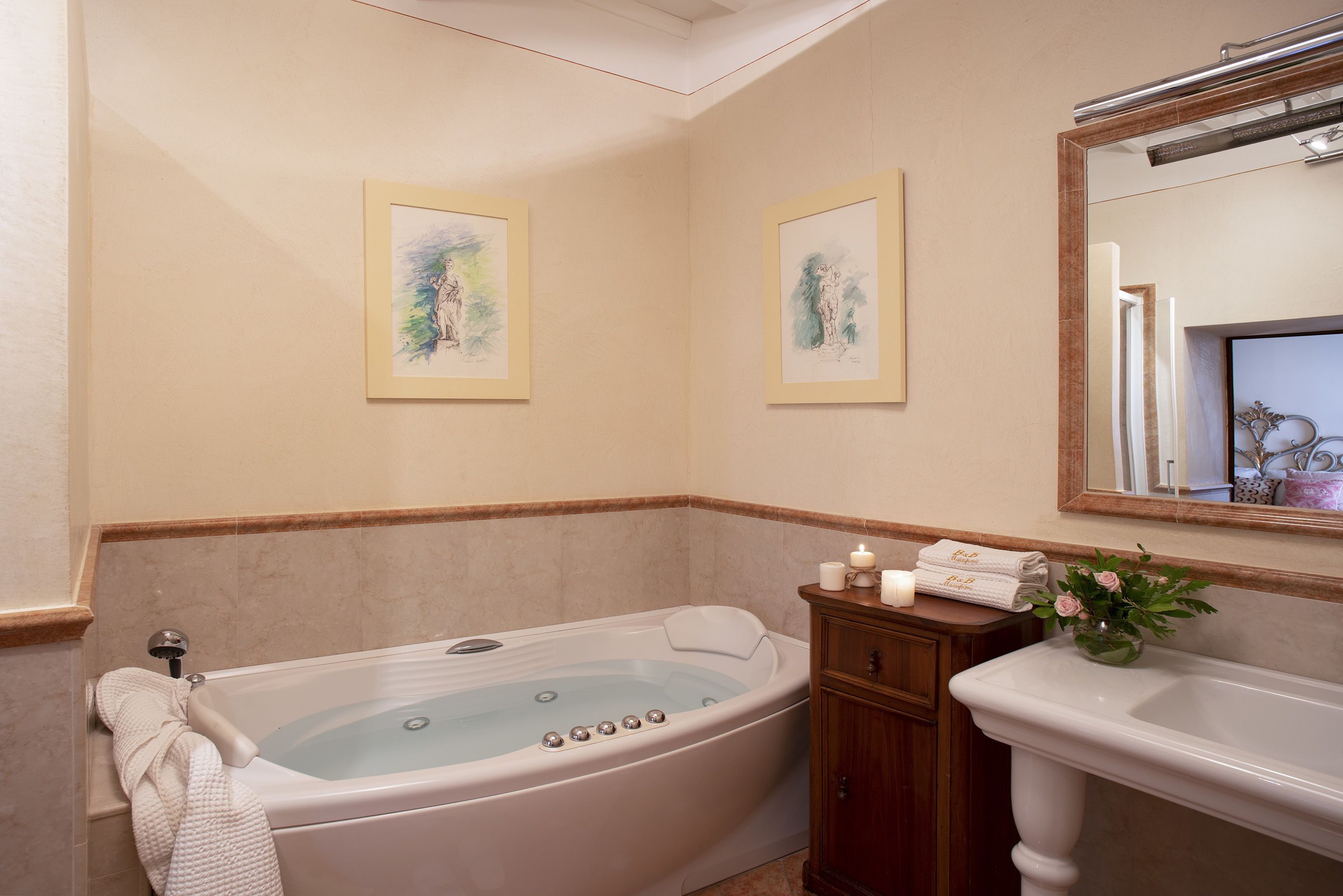 Ein Badezimmer mit einer Badewanne, einem Waschbecken, einem Spiegel, gerahmten Kunstwerken und einer Blumenvase.