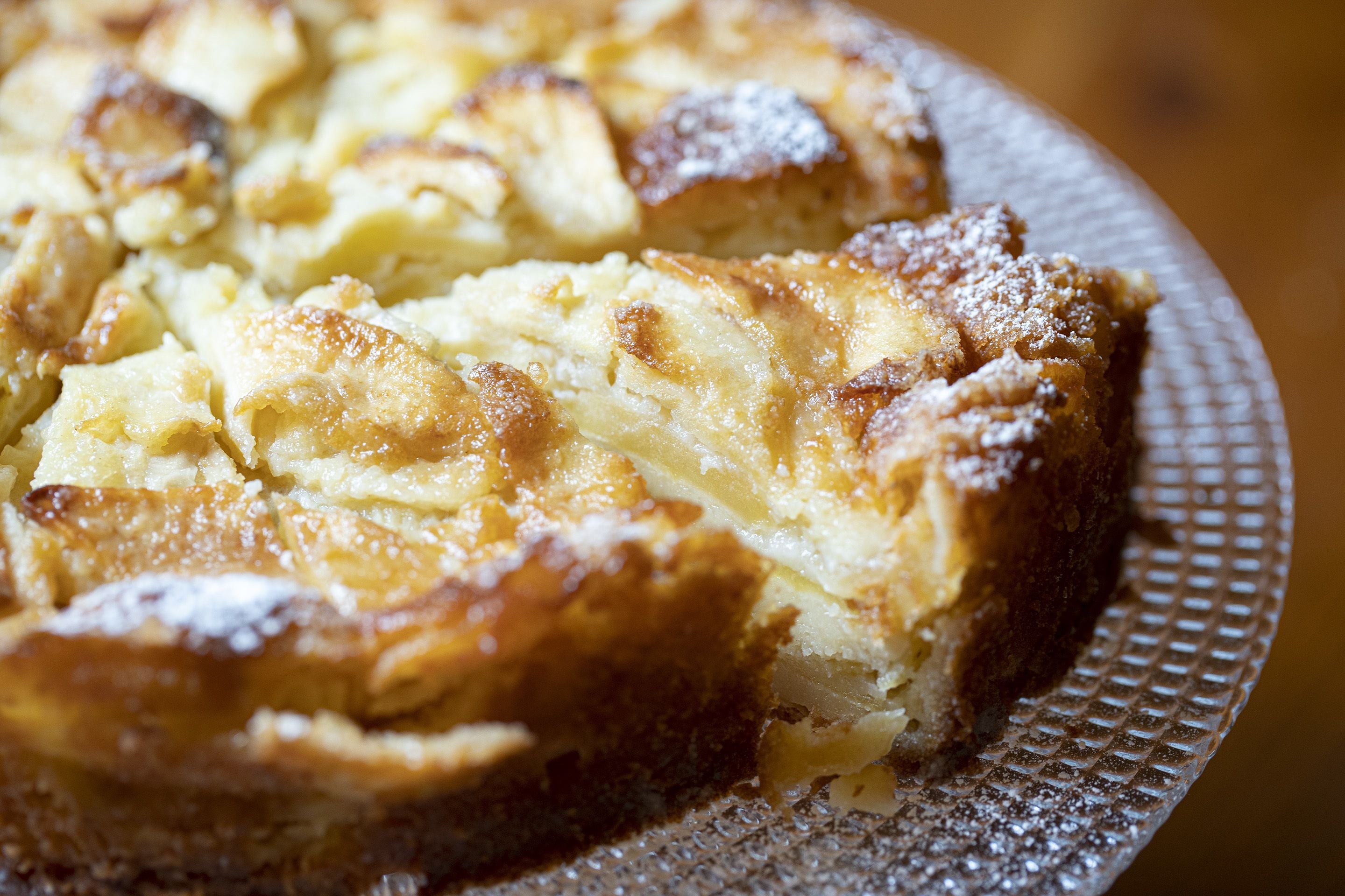 Ein Nahaufnahme von einem Dessert mit goldbrauner Kruste, bestäubt mit Puderzucker, auf einem strukturierten Teller.