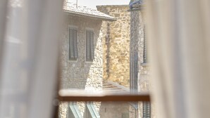 A narrow street with stone buildings, a person walking, and a door with a window. - Palazzo Malaspina (Barberino Tavarnelle)