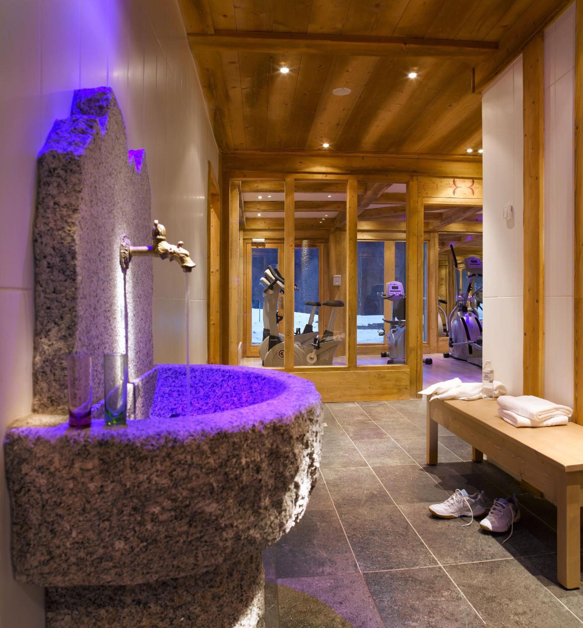 A stone basin with a faucet, a bench, and exercise equipment in the background.