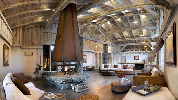 Un intérieur spacieux avec un haut plafond en bois, une cheminée en pierre et des coins salon confortables.