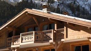 Un chalet en bois doté de plusieurs balcons, situé au pied d’une montagne enneigée.