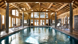 Une piscine intérieure dotée de poutres en bois et de piliers en pierre, entourée de grandes fenêtres.