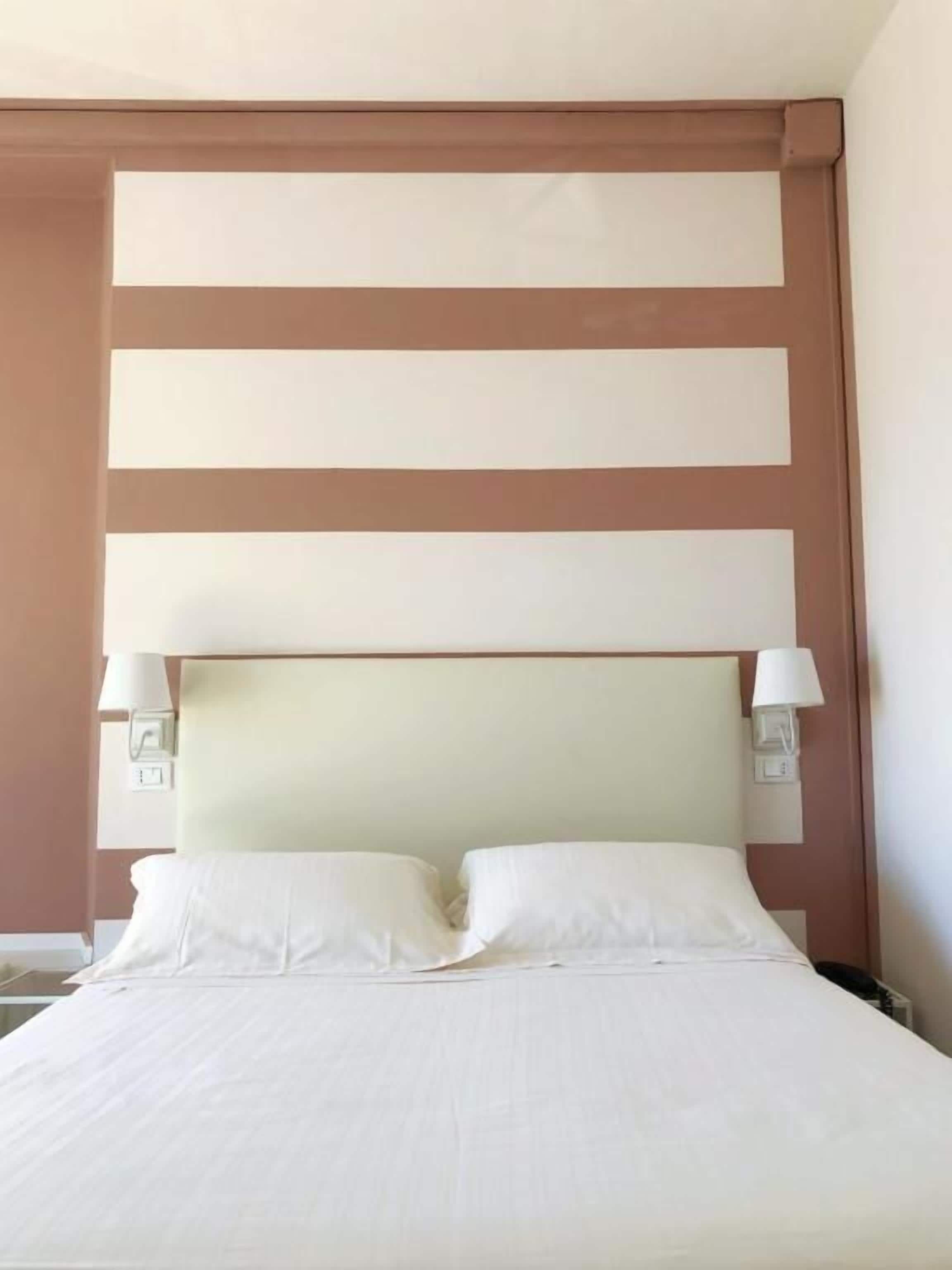 A hotel room with a bed, two bedside lamps, and a headboard with horizontal panels.