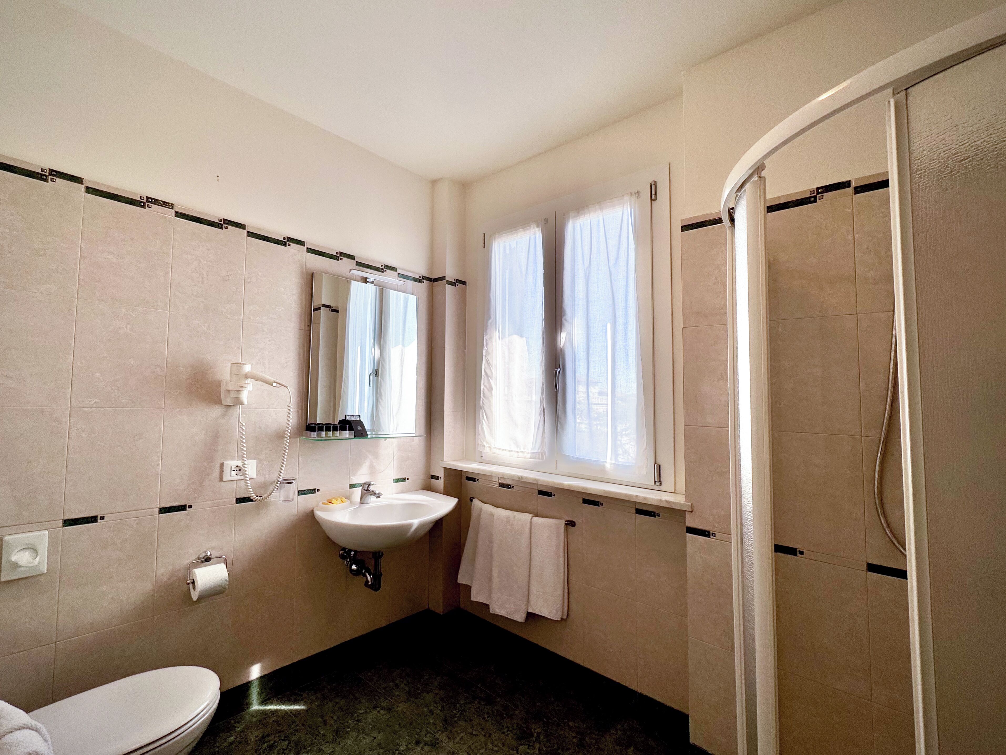 A bathroom with a toilet, sink, mirror, and shower.