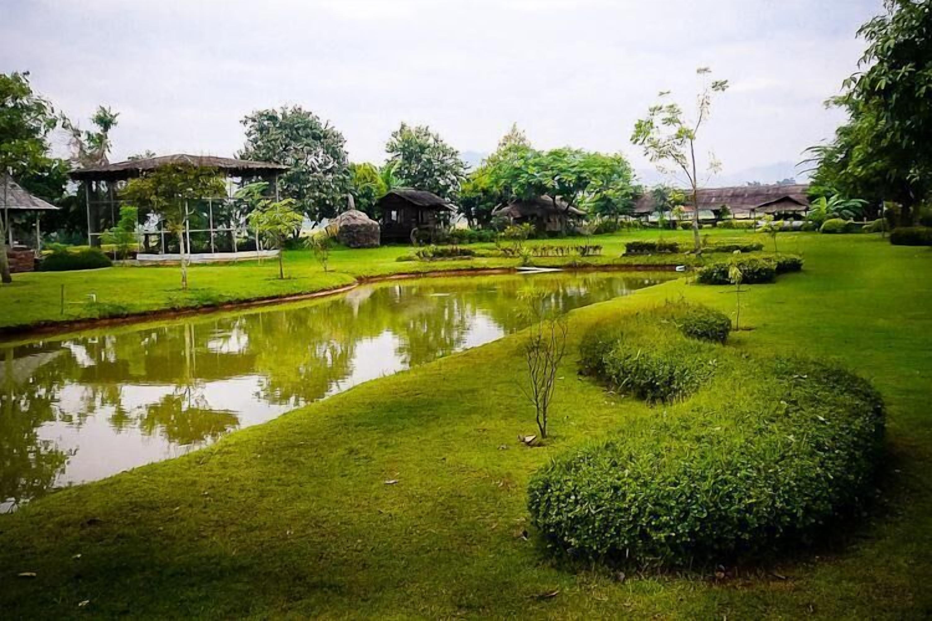 A serene garden with a pond, neatly trimmed grass, and traditional huts.