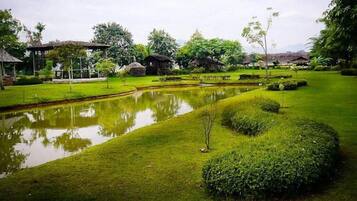 A serene garden with a pond, neatly trimmed grass, and traditional huts.
