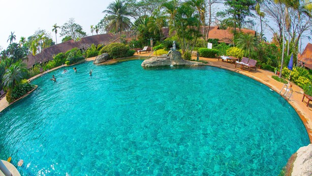 A large, clear blue pool with a rock centerpiece, surrounded by lounge chairs and palm trees. - Golden Pine Resort (Chiang Rai)