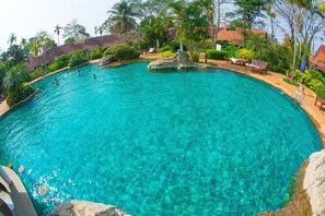 A large, clear blue pool with a rock centerpiece, surrounded by lounge chairs and palm trees. - Golden Pine Resort (Chiang Rai)