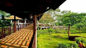 A covered walkway with a patterned floor, surrounded by lush greenery and a small bridge in the background. - Golden Pine Resort (Chiang Rai)
