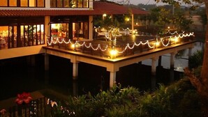 A two-story building with a red-tiled roof, a dock extending into a body of water, and string lights along the dock. - Golden Pine Resort (Chiang Rai)